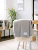 A soft, neutral grey wool throw, by Ruanui Station, in a pretty chevron pattern, shown draped over a chair