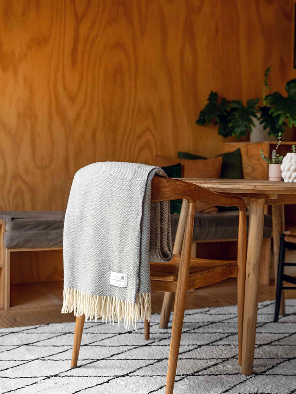 A soft, neutral grey wool throw, by Ruanui Station, in a pretty chevron pattern shown draped over a chair in a modern living space