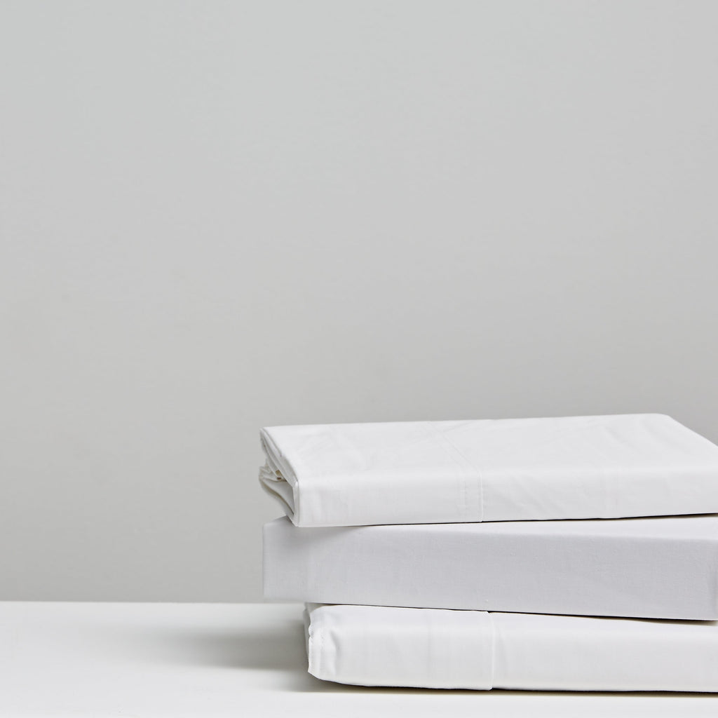 Three folded white 100% cotton bedding pieces stacked neatly on a white surface 