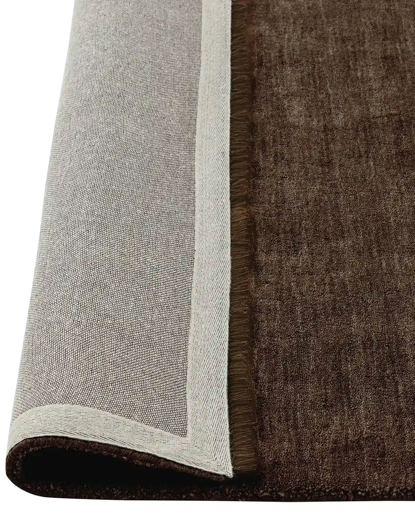 The Silvio wool rug by Weave Home in a ruich chocolate brown tone called Dovecote, rolled to show underneath