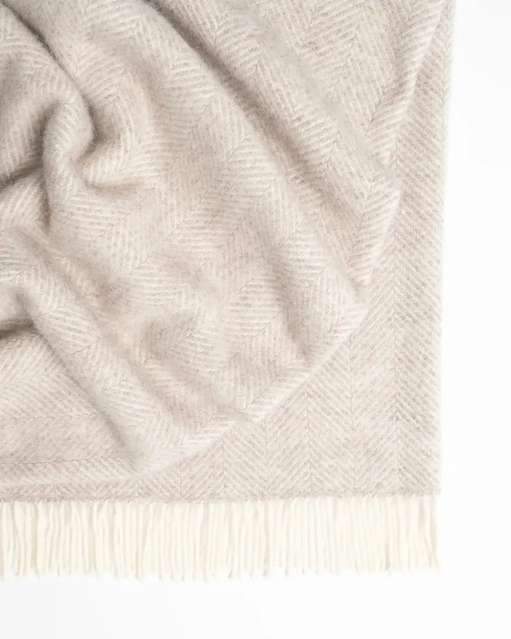 A light, dusty pink with off-white wool herringbone throw blanket with fringe