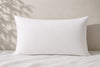 A plain white 100% cotton long lodge style pillow resting on white bedding 