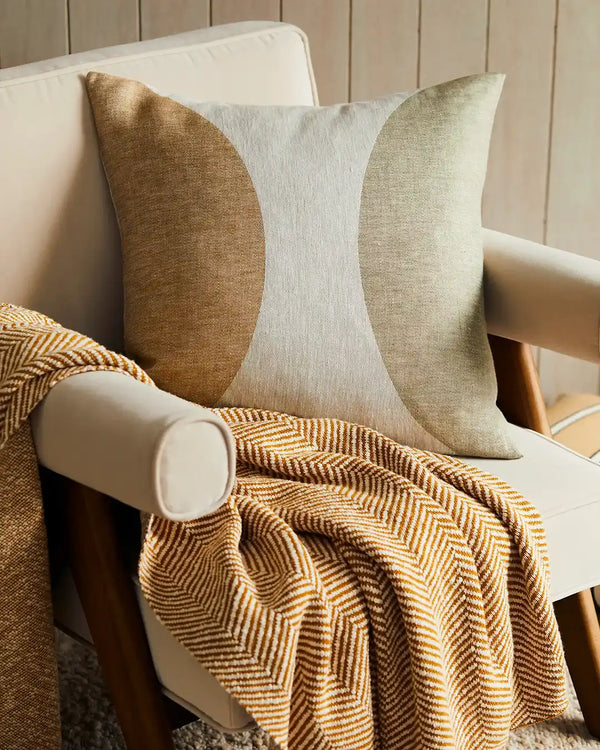 Weave Home Halcyon cushion featuring a nostalgic geometric in mustard and olive, displayed on a chair with the Solano Amber throw blanket