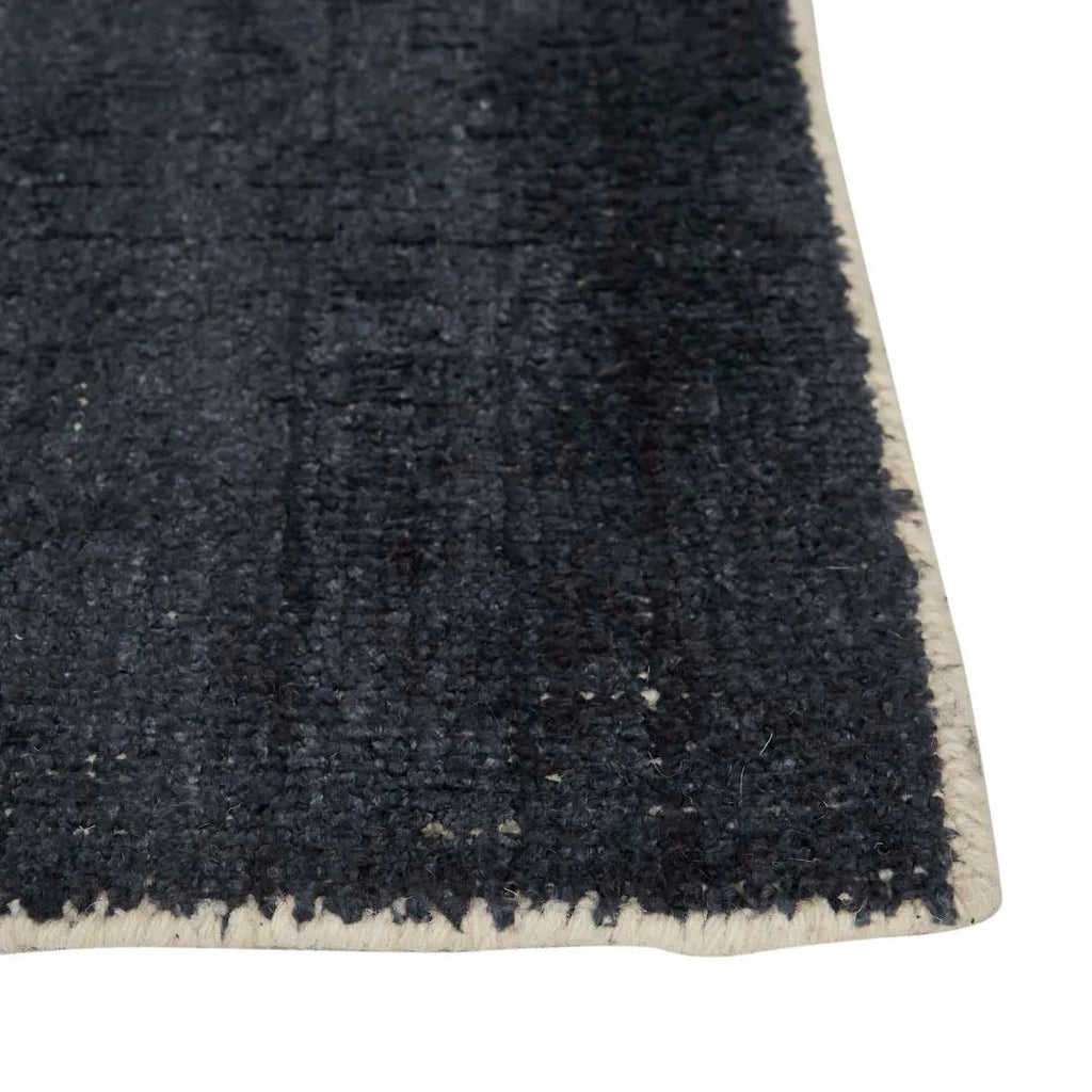 Close up of the corner of a dark blue wool blend floor rug to reveal weave and edge border
