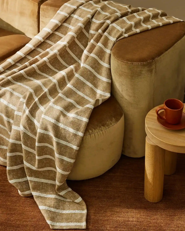 Light brown and white striped throw draped over a brown velvet couch
