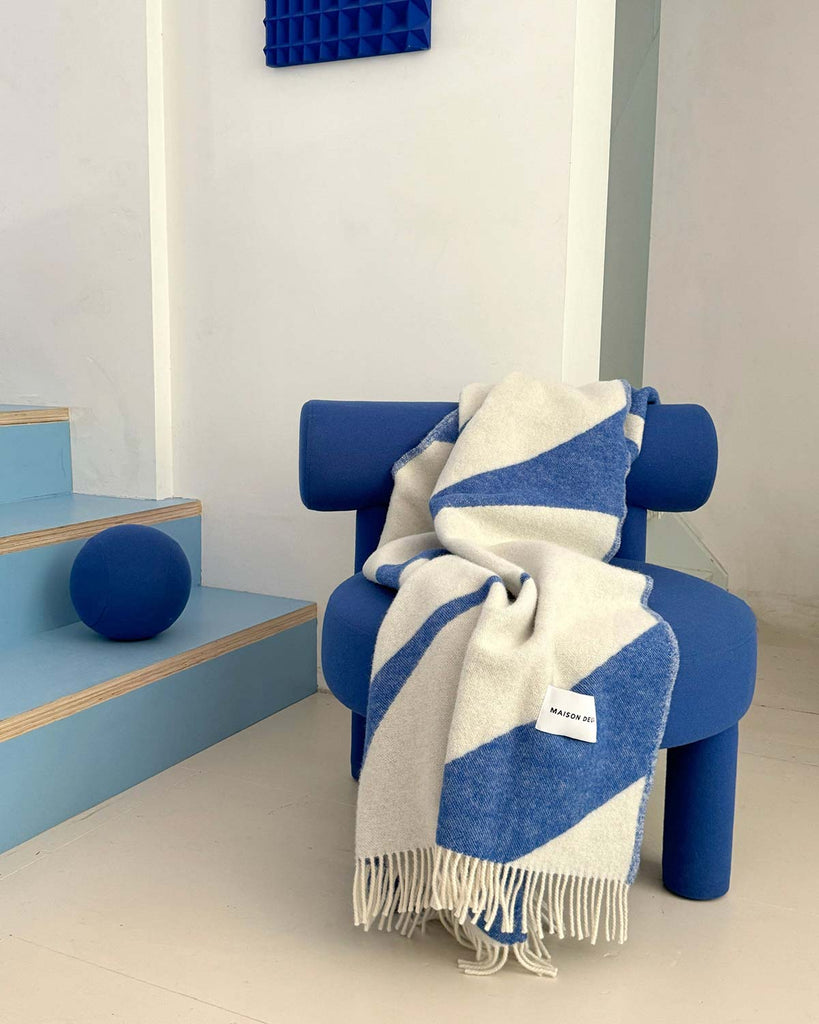A Maison Deux blue and white swirling patterned throw draped over a chair in a stylish, cobalt toned room. 