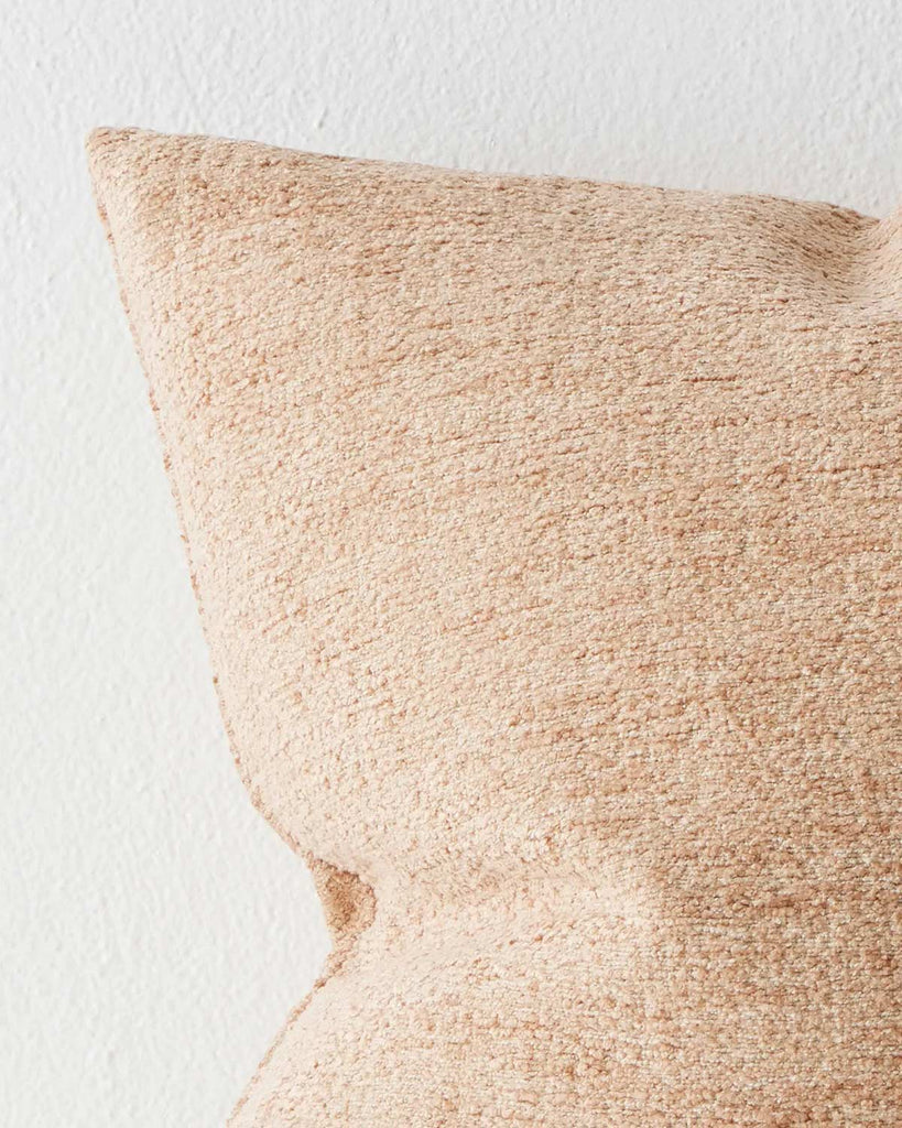 The corner of a textured cushion in soft clay tones. 