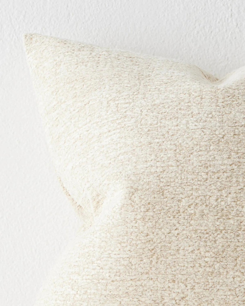 A close up image of an off-white warm toned cushion with a soft texture in the weave. 