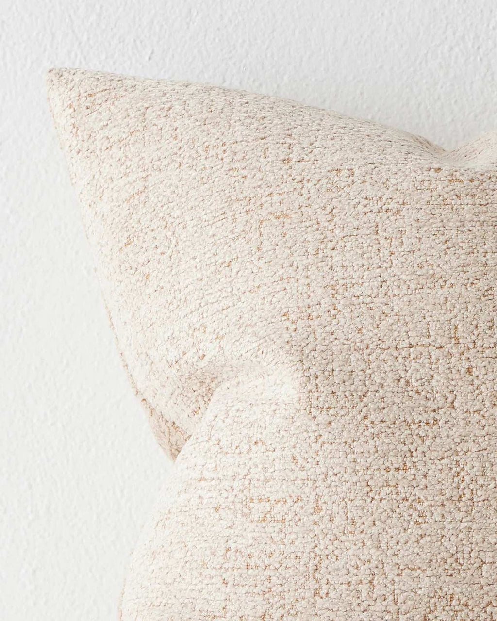 The corner of a soft textured cream toned cushion with brown undertones. 