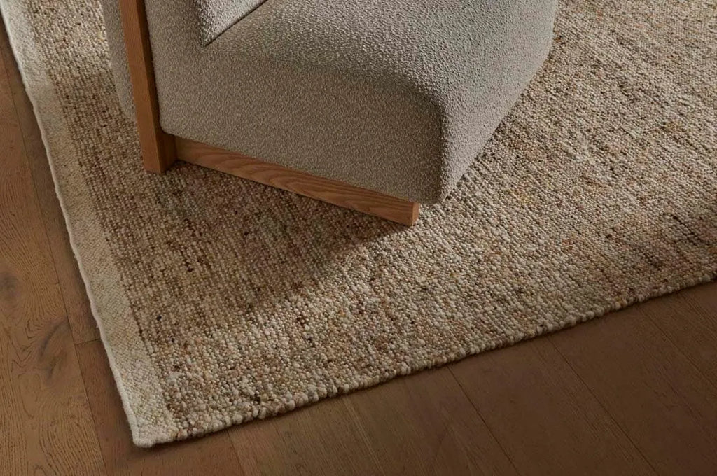A textural woolen rug, in shades of honey brown and light beige, with subtle colour shifts by Soren Liv NZ and Globe West, underneath a designer chair. 