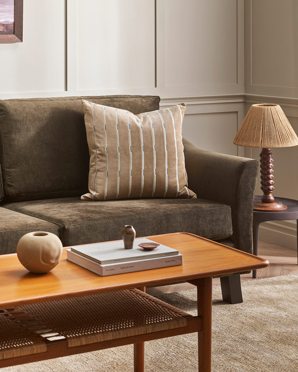 A soft velvet textured cushion in shades of sandy brown with a linear pattern, on a couch in a modern living room. 