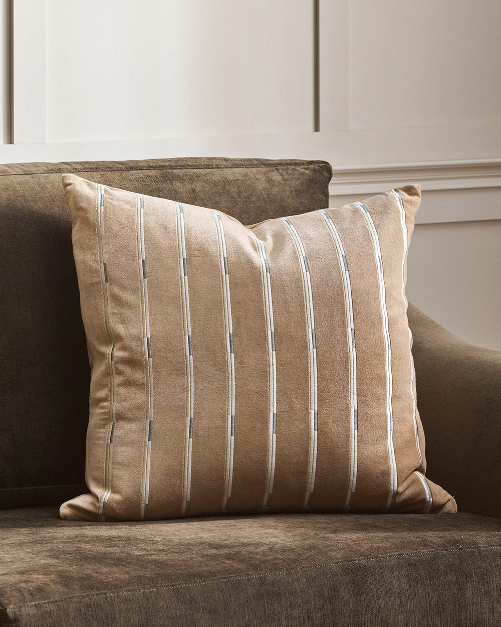 A close up image of a soft neutral brown velvet cushion with an embroidered linear pattern. By Baya. 