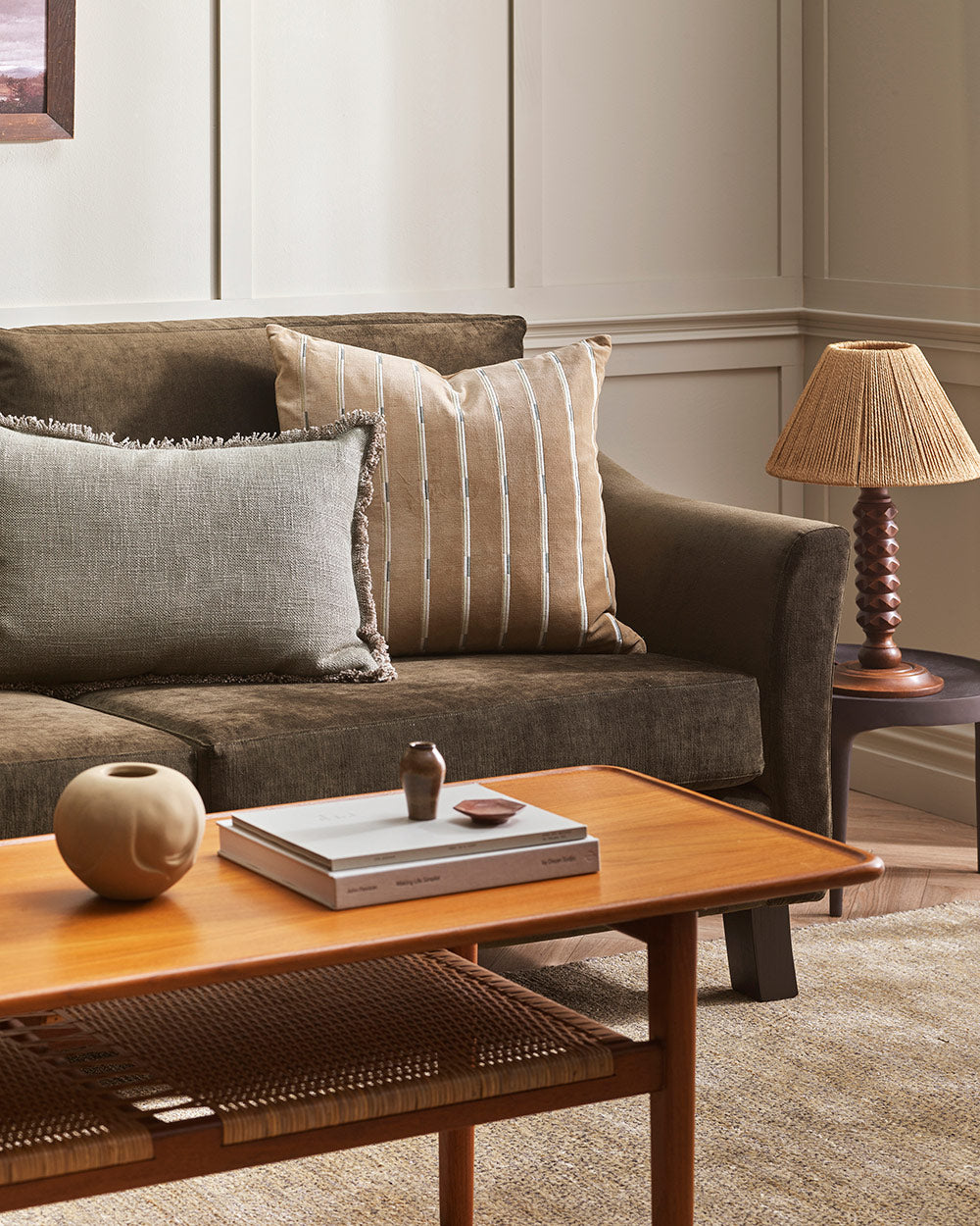 A stylish living room in warm earth tones with a striped velvet cushion in a shade of brown-beige on the couch. 