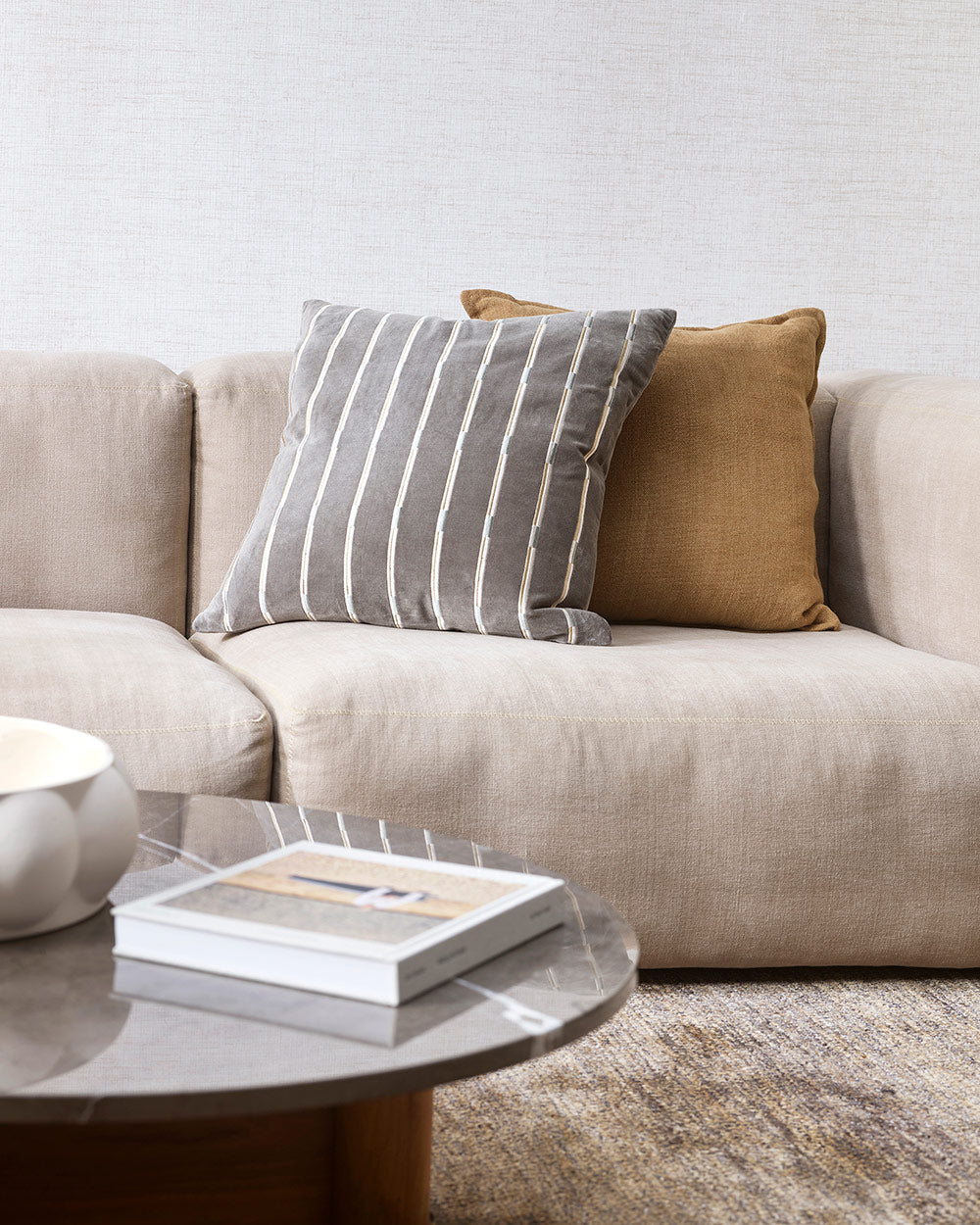 A modern style living room with a cream couch and a patterned velvet cushion in slate grey and white. 
