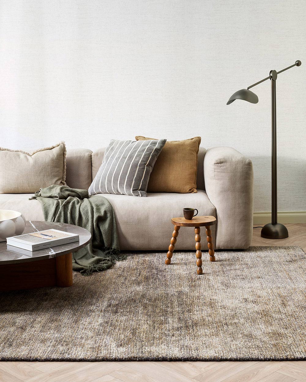 A modern stylish living room with a green grey wool floor rug and a complimentary cushion on the couch, in slate grey. 