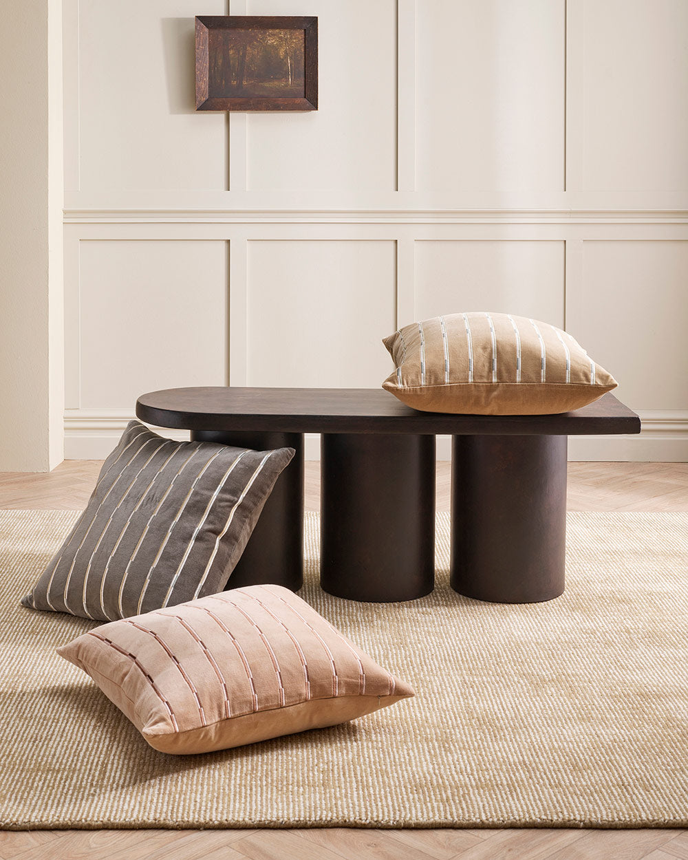 Three cushions on and around a coffee table, all with a gorgeous striped linear velvet pattern but with different colours— one is slate grey, one a warm beige brown and one a muted clay pink. 