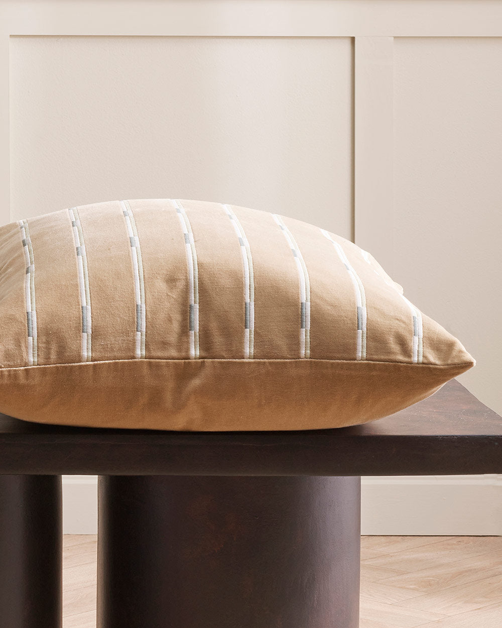 A close up image of a velvet textured cushion with a linear striped cushion in warm brown. 