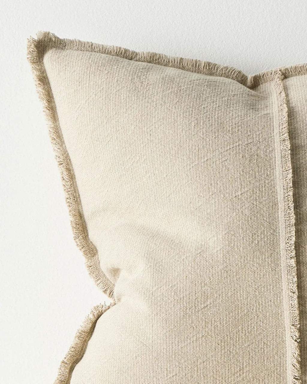 Close up of a beige cushion with textured trim on a light background