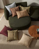Green round ottoman with various colored cushions on a beige rug.