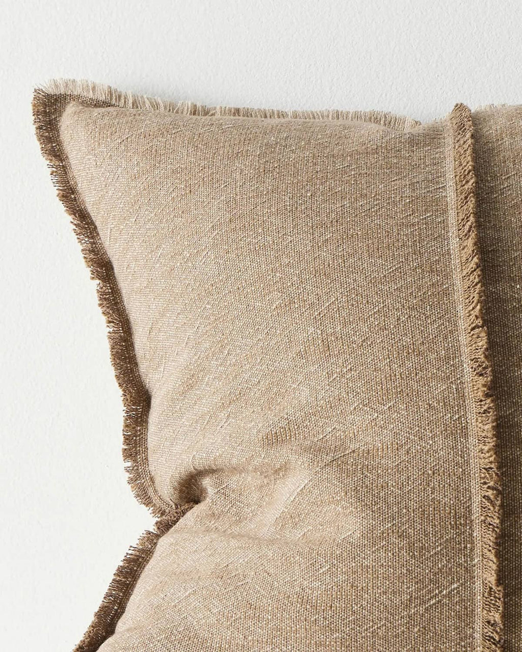 Close-up of a textured beige pillow with frayed edges on a light background