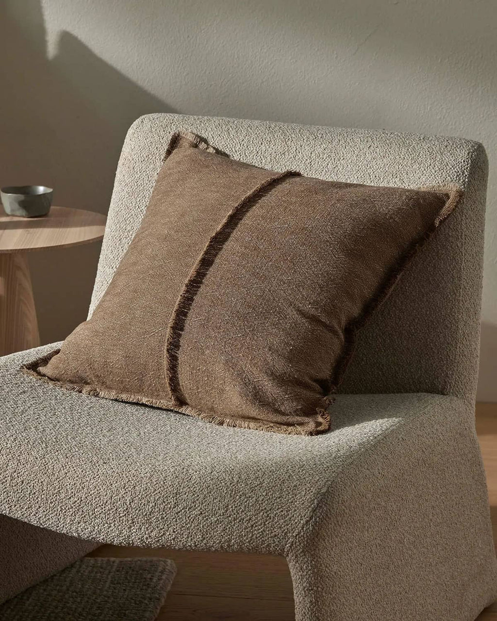 Brown textured pillow on a textured chair with a neutral background