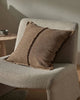 Brown textured pillow on a textured chair with a neutral background