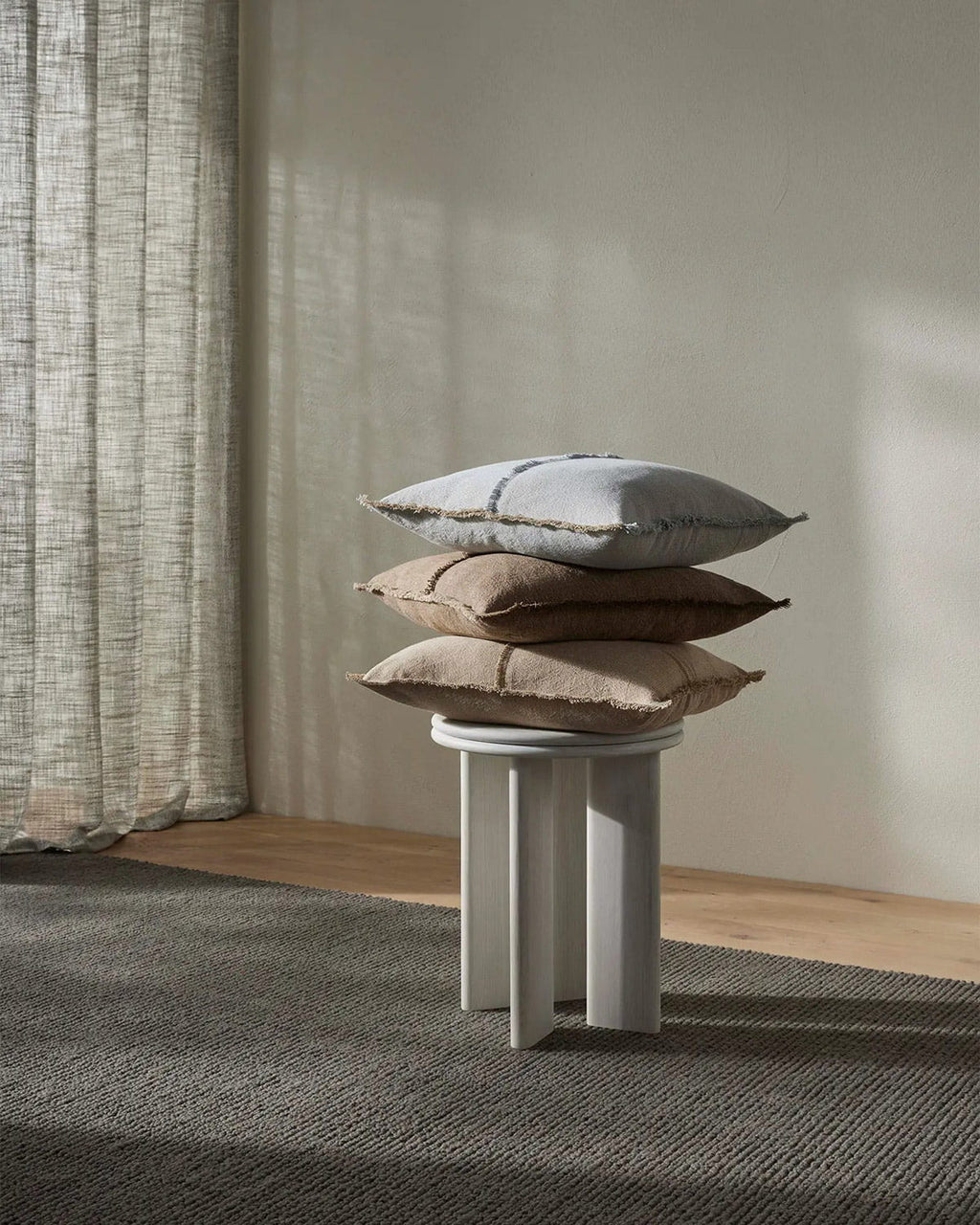 Stack of pillows on a small round table against a neutral wall with curtains.