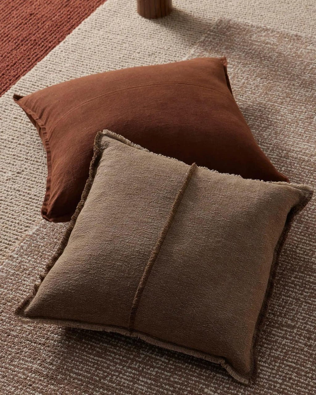 Two brown cushions on a textured floor rug