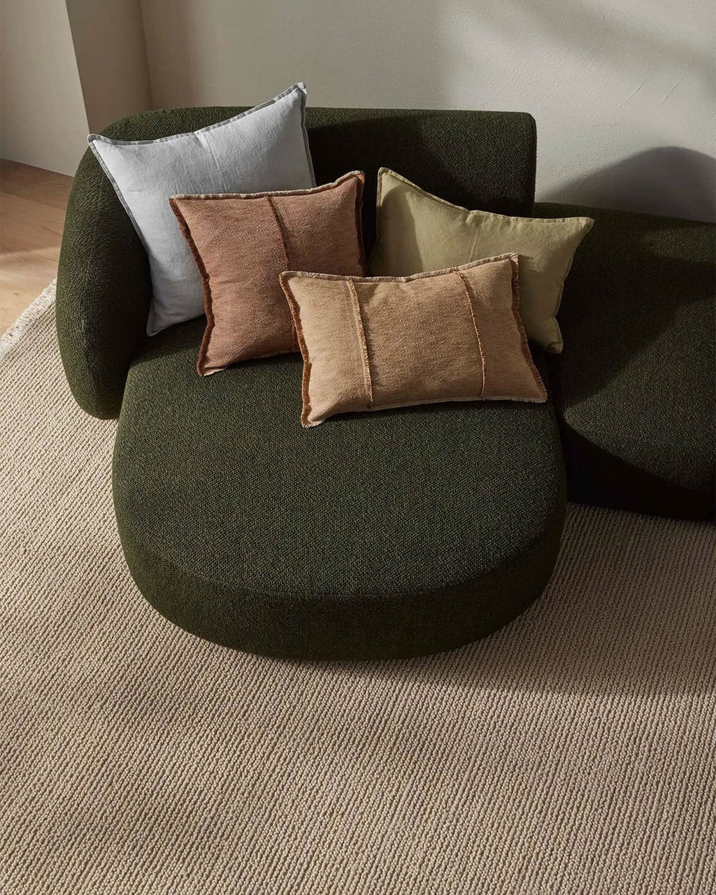 Green curved sofa with colorful cushions on a neutral carpet
