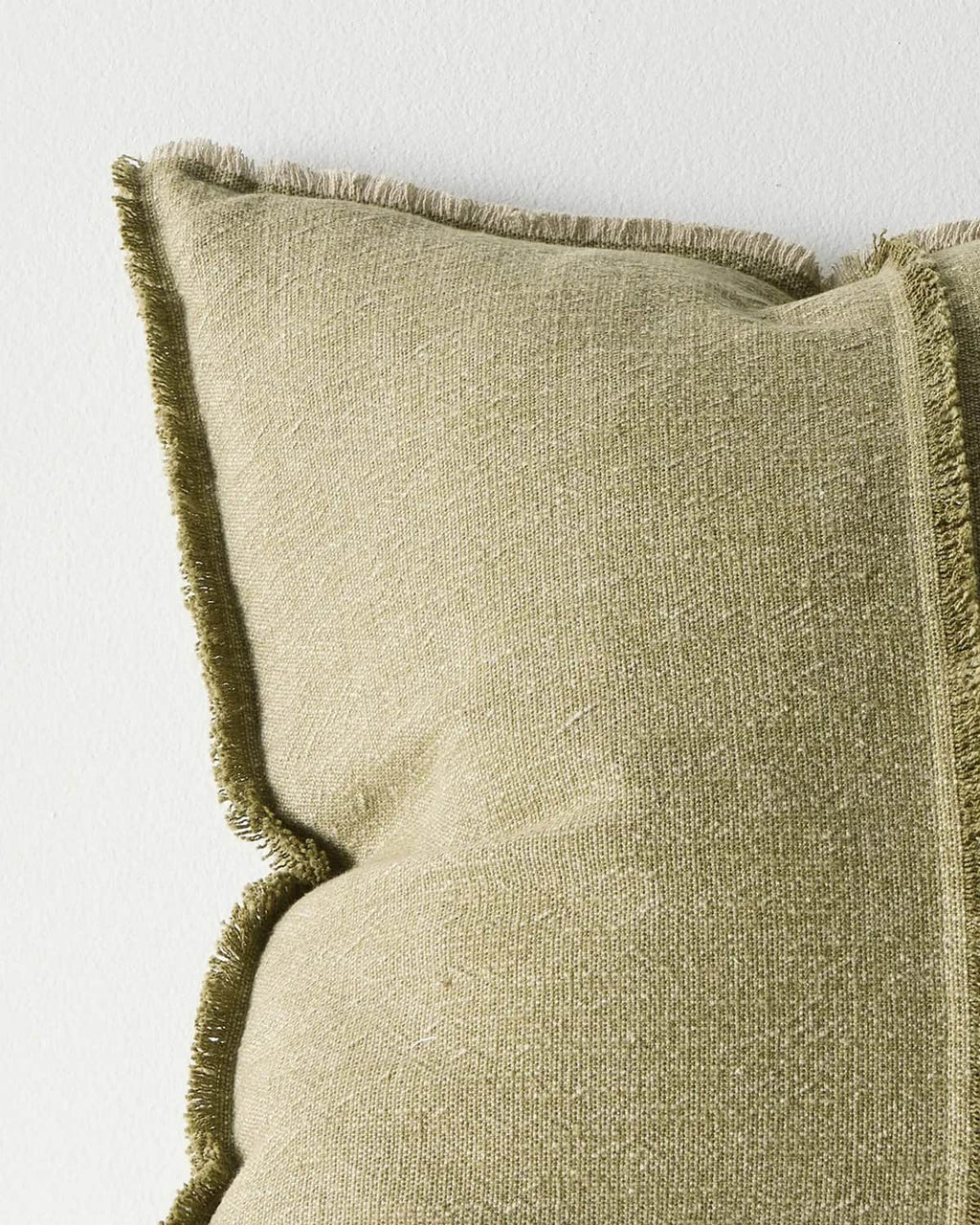 Corner of a textured green cushion with frayed edges on a light background