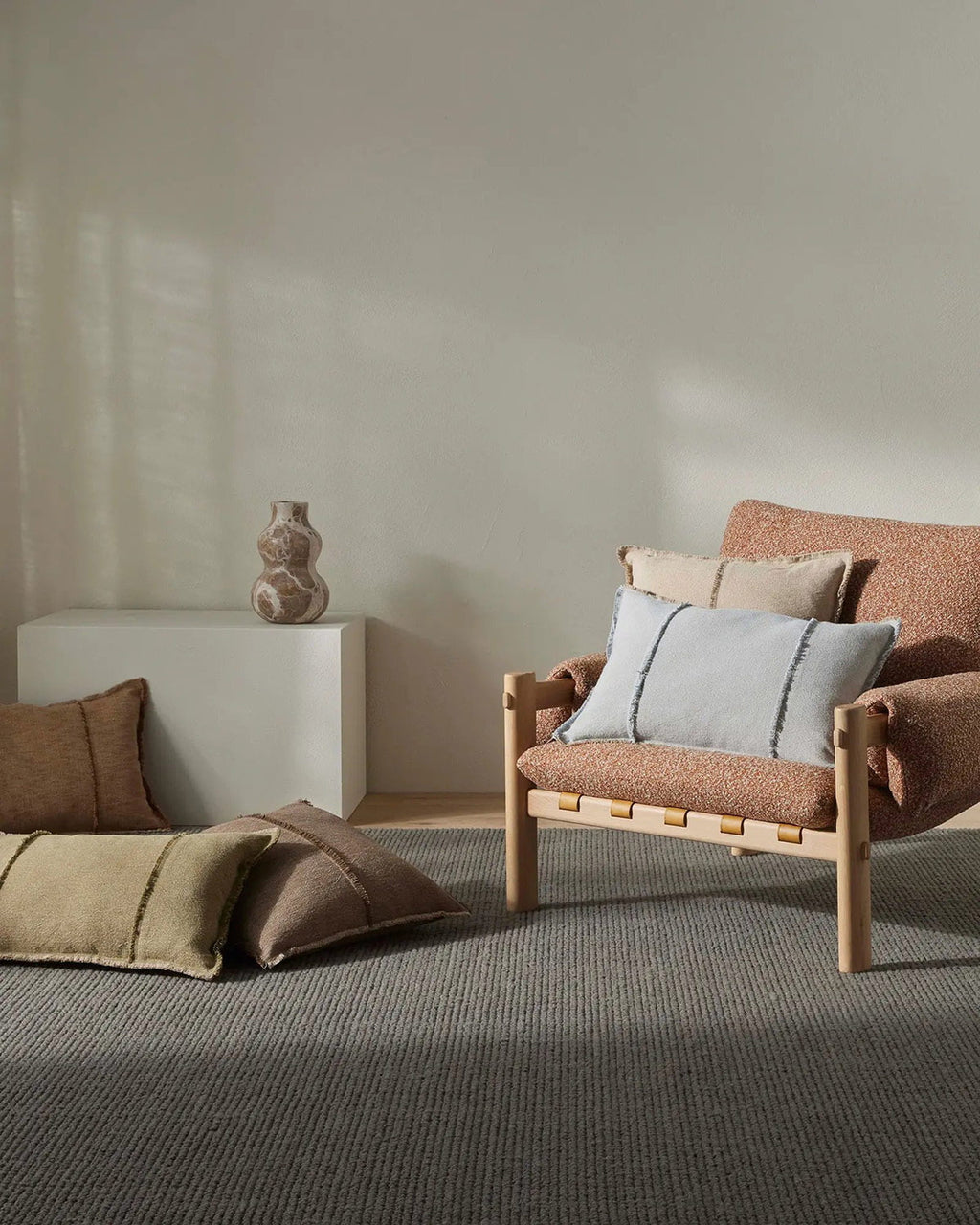 Modern living room with a brown armchair and decorative pillows against a neutral wall.