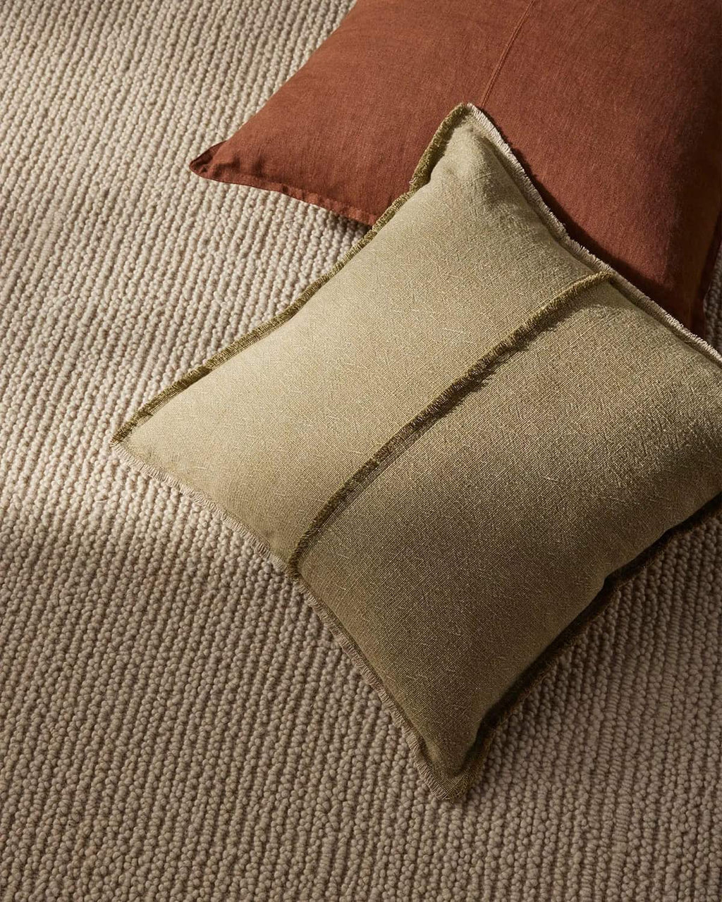 Green pillow on a textured surface with a brown pillow in the background