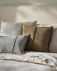 Three pillows in gray, beige, and green on a textured bed against a textured wall.