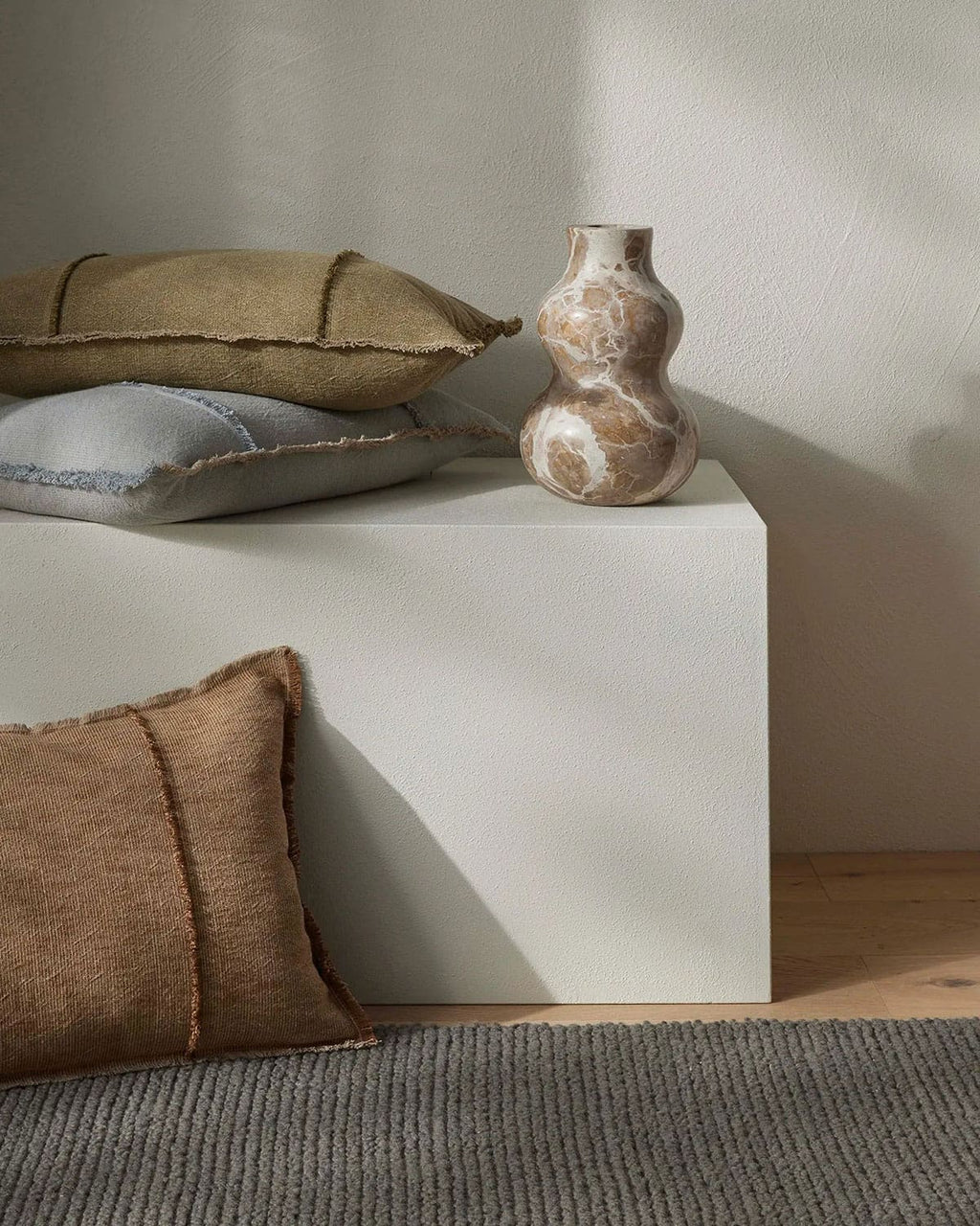 Decorative pillows and a vase on a white surface with a neutral background