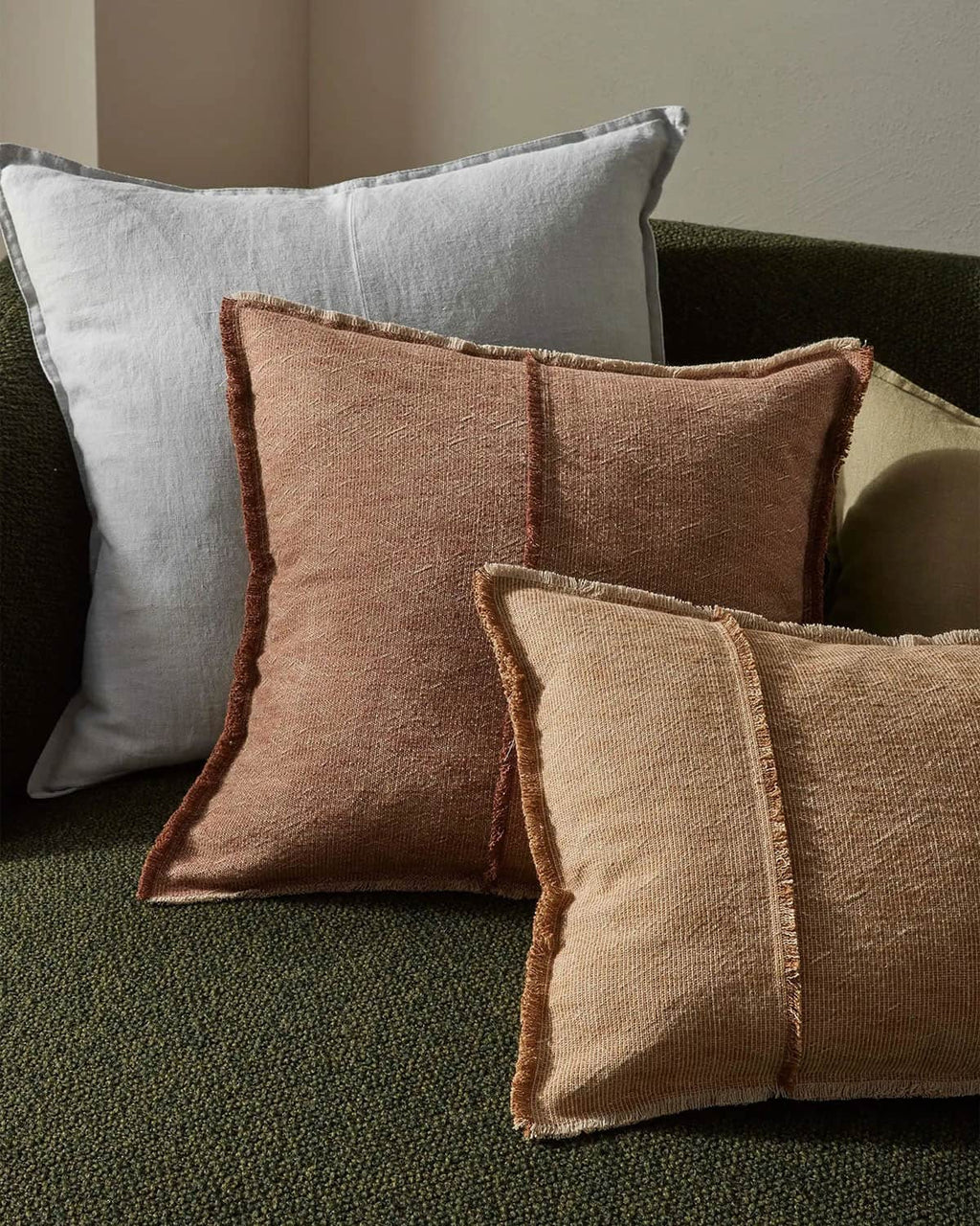 Three textured pillows in brown and gray on a green sofa.