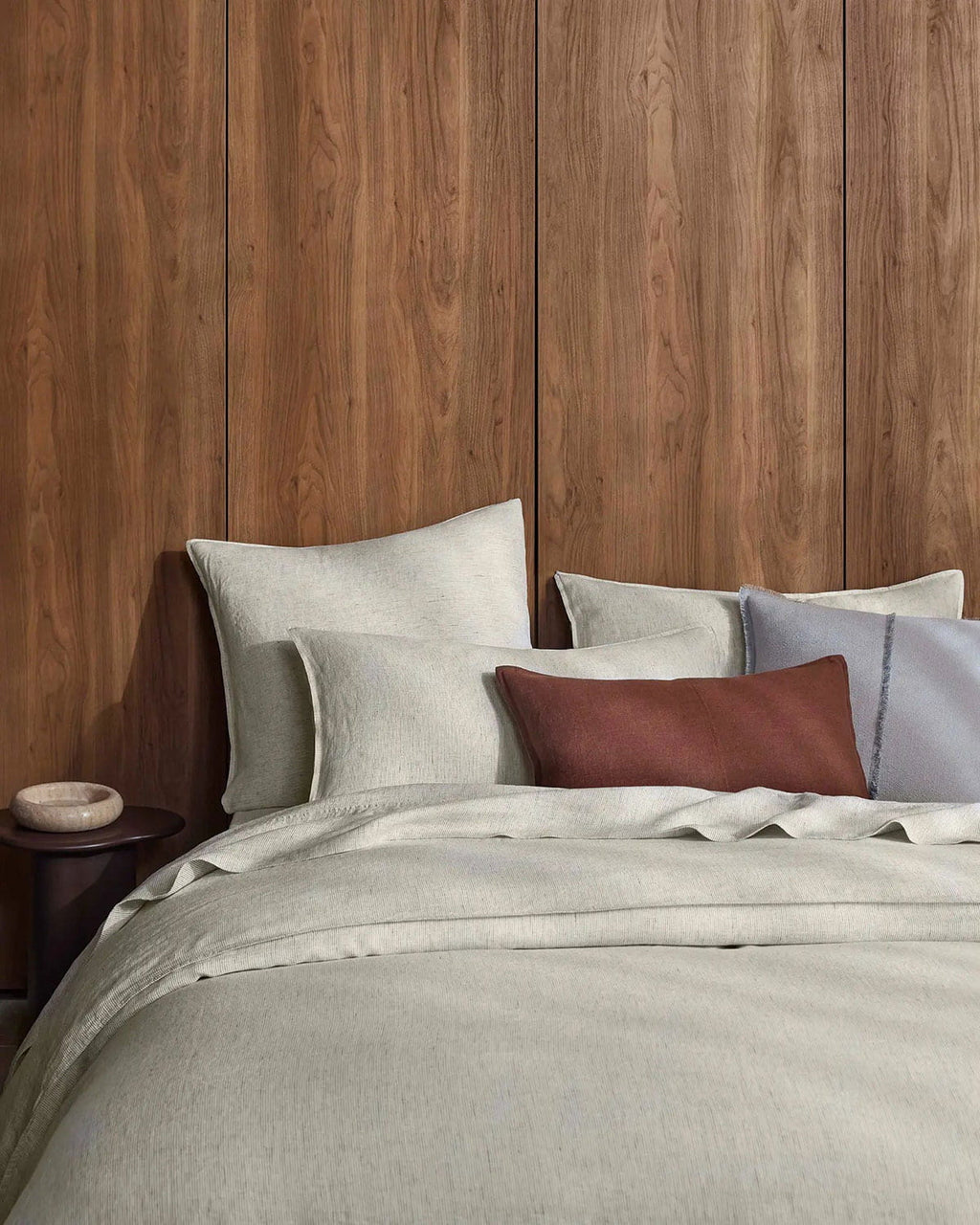 Neatly made bed with gray bedding against a wooden wall.