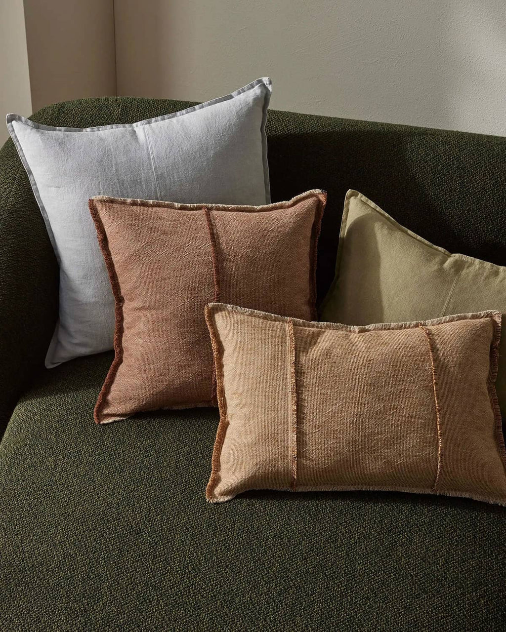Set of four textured pillows in various colors on a green sofa.