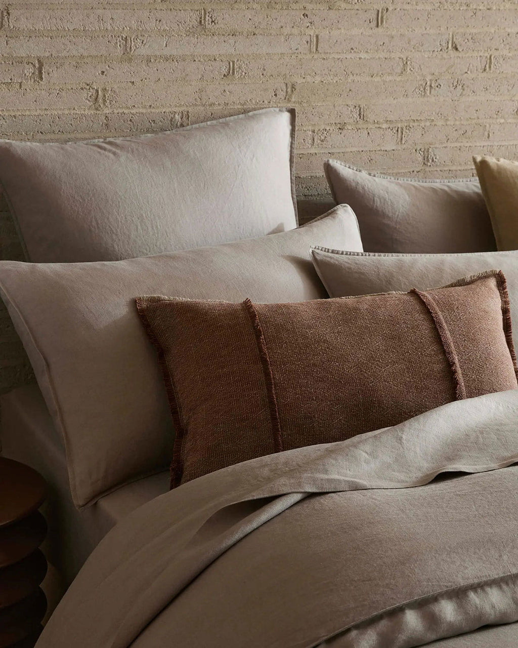 Neatly arranged pillows on a bed with a textured wall in the background