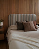 Bed with striped headboard and brown pillows against a wooden wall.