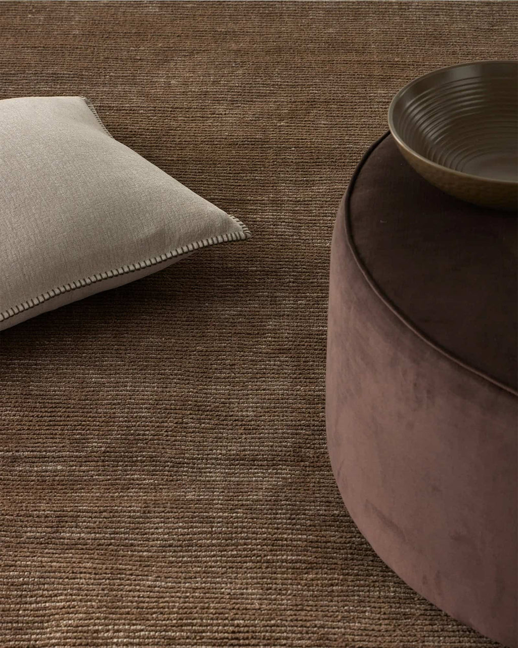 Textured brown rug with a beige Weave Home 'Alba' cushion and bowl on top