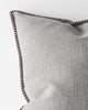 Close up corner of a grey textured cushion with a dark brown stitch detail on a light grey background