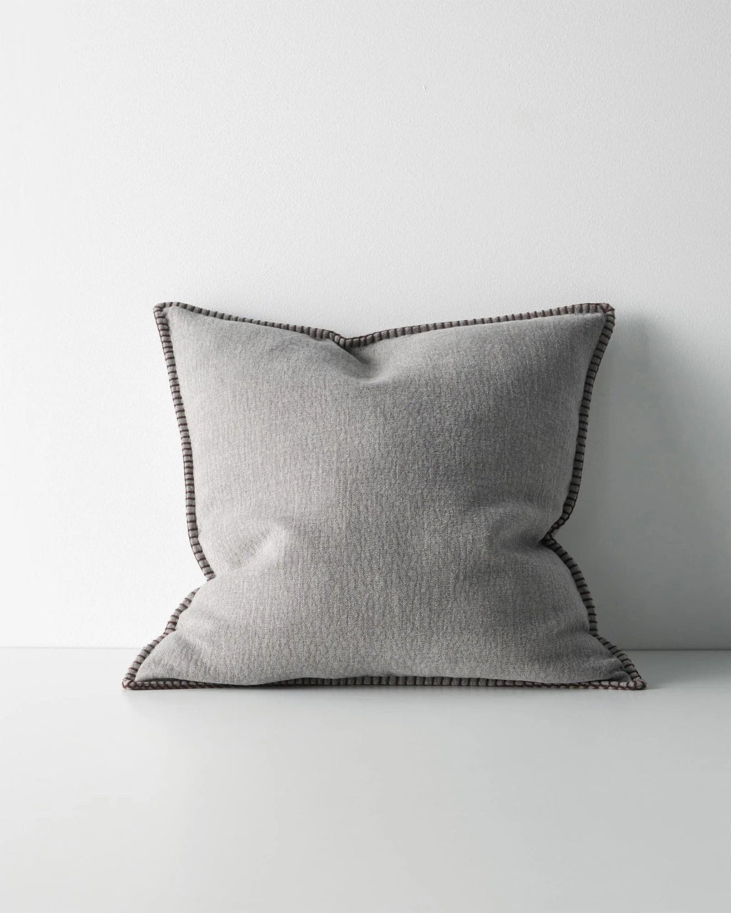 Grey textured cushion with a dark brown stitch detail on a light grey background