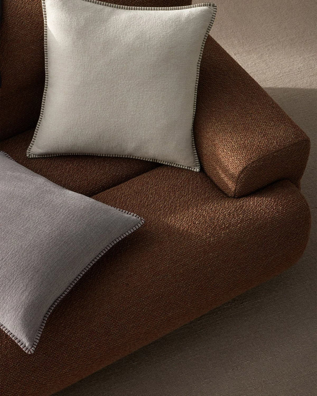 Brown sofa with two grey Weave Home cushions on a neutral background