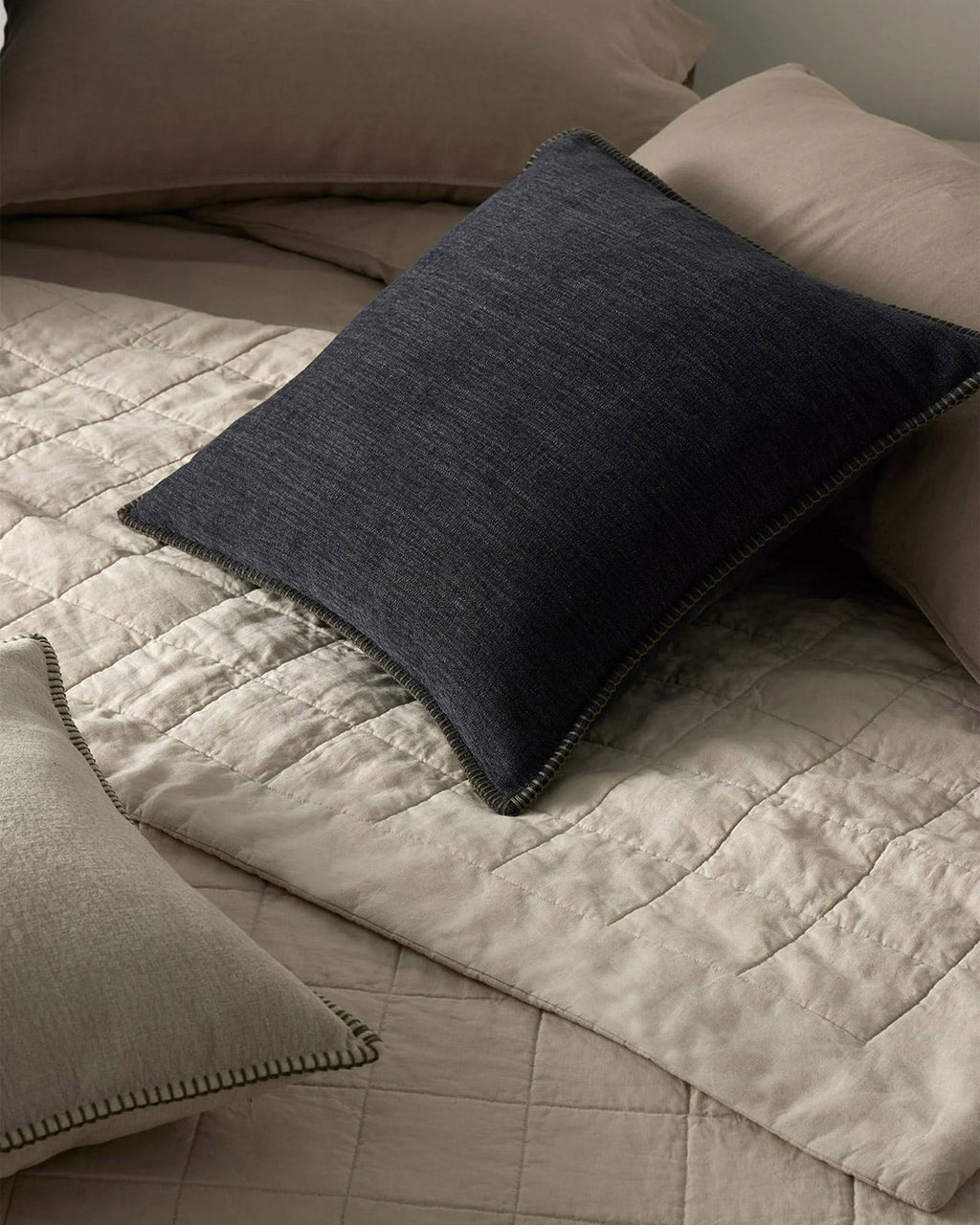 Dark blue pillow on a beige quilt with neutral pillows in the background