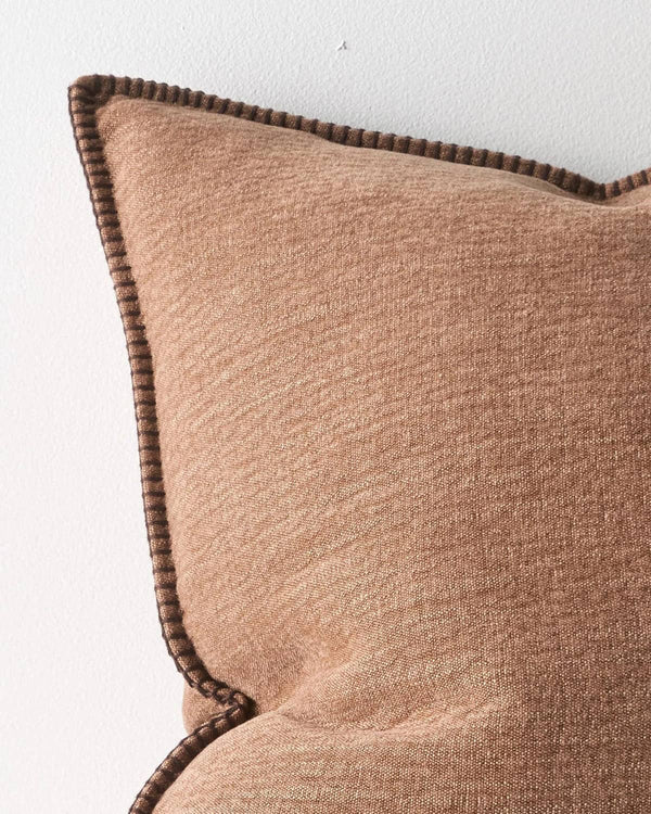Close up of a brown cushion with a textural fabric and elegant stitching detail on a white background