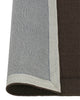 A Chocolate brown NZ wool floor rug with cut border, by Weave Home, with edge rolled to show underlay