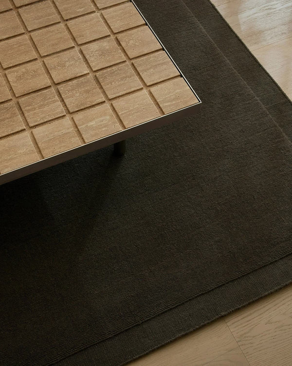Close-up of a wooden table surface looking down on a chocolate brown wool floor rug