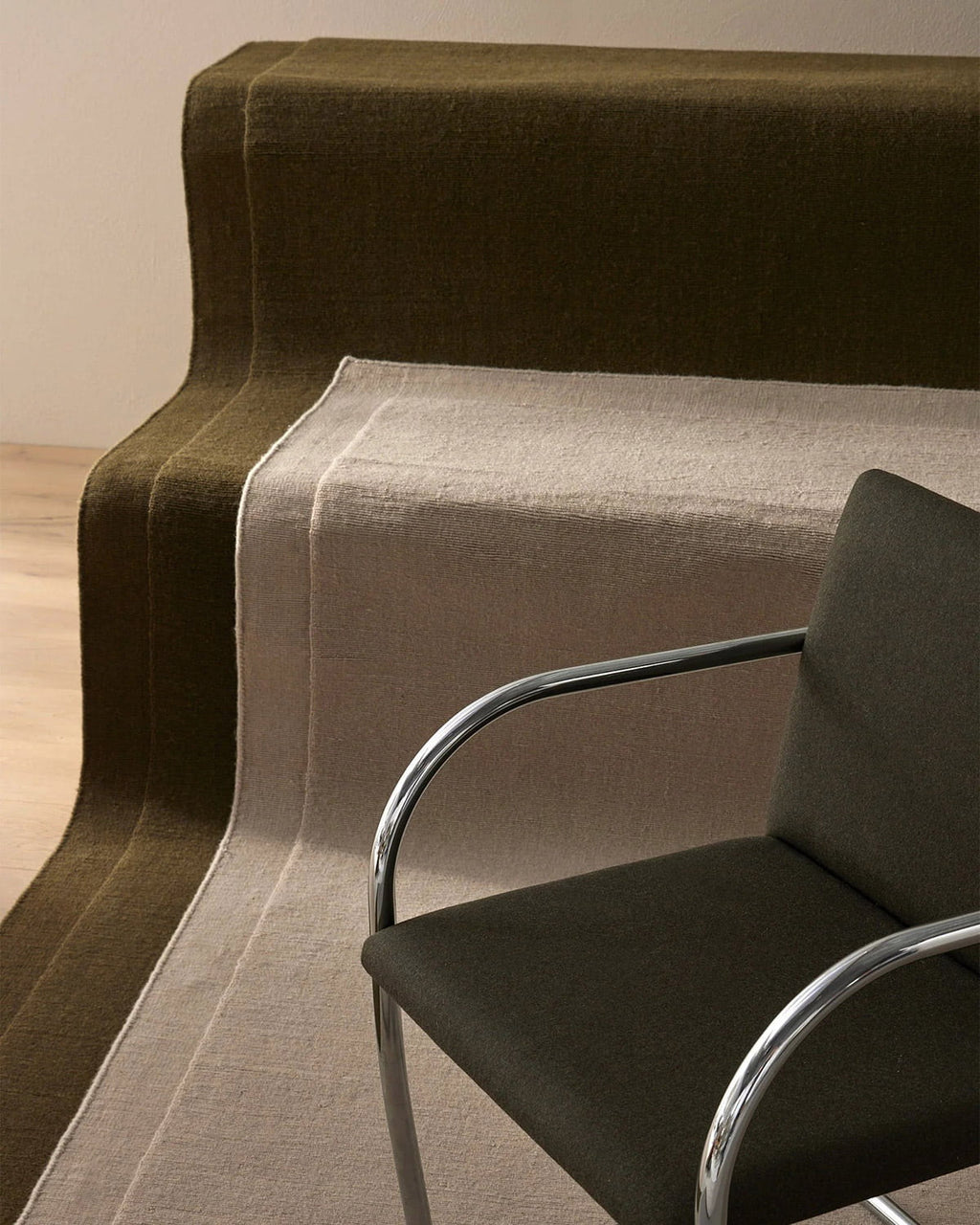  The Cassio Jasper NZ wool floor rug in a deep olive shade laid out on stairs with a beige rug and chair