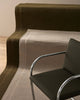  The Cassio Jasper NZ wool floor rug in a deep olive shade laid out on stairs with a beige rug and chair