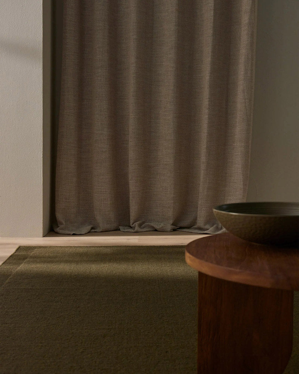 Brown curtain in a room with a wooden table and bowl and a designer wool rug